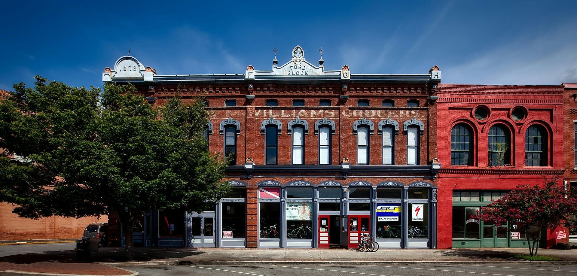 Brick buildings with storefronts line a sunny street, vibrant blue sky above.