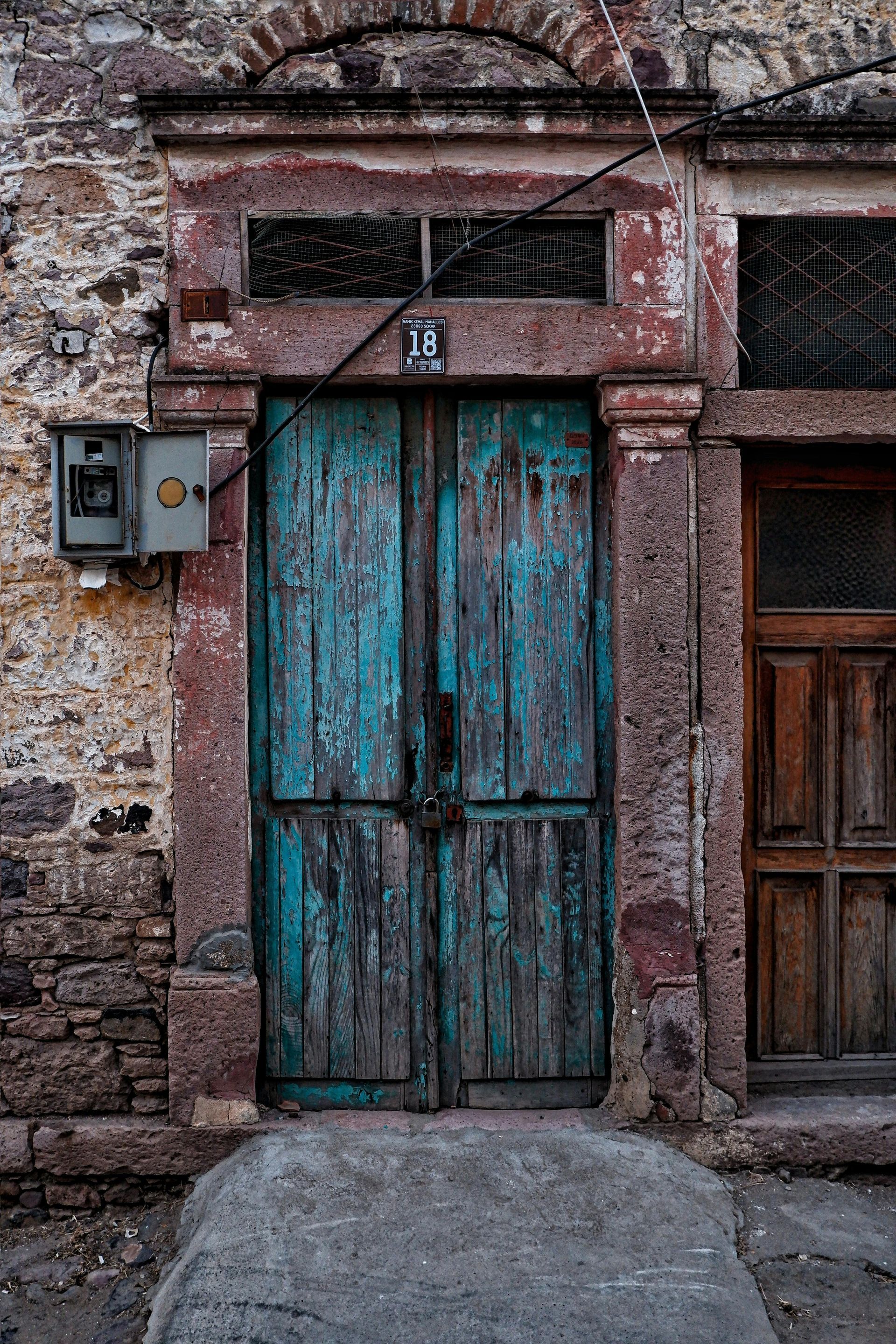 Weathered turquoise door in a stone building, framed by faded red trim.
