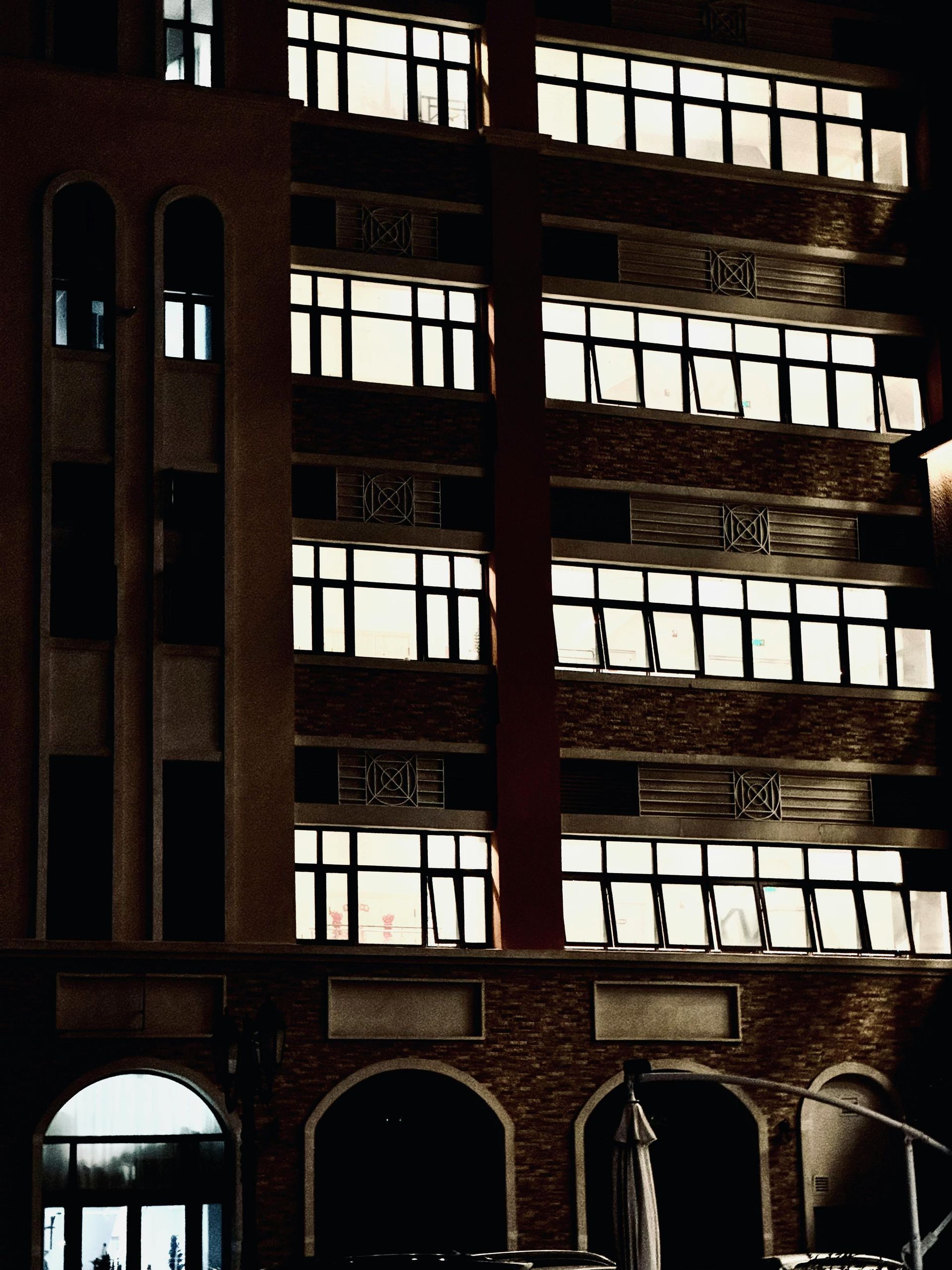 Brick building at night with lit windows. A figure in a long coat stands in front of the entrance.