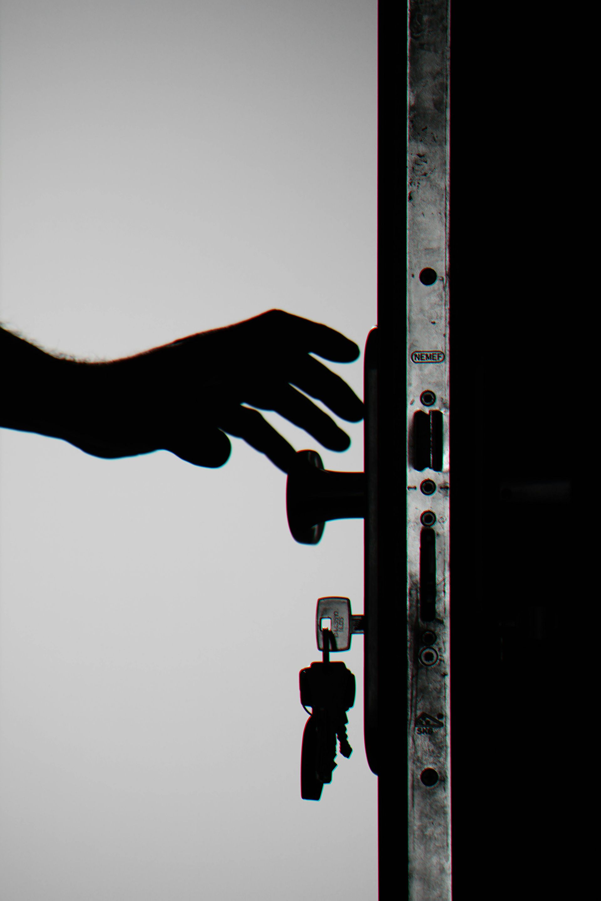Silhouette of a hand reaching for a doorknob on a dark door with keys in the lock, contrasting against a bright background.