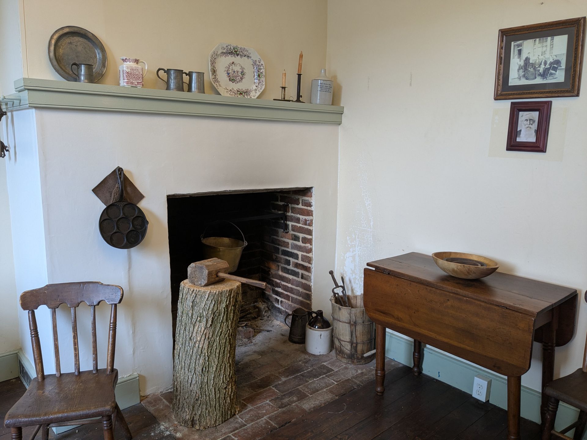 A colonial-era room with a fireplace, table, chair, and kitchenware.