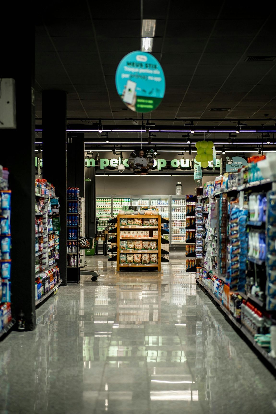 A very long aisle in a grocery store with a sign hanging from the ceiling.