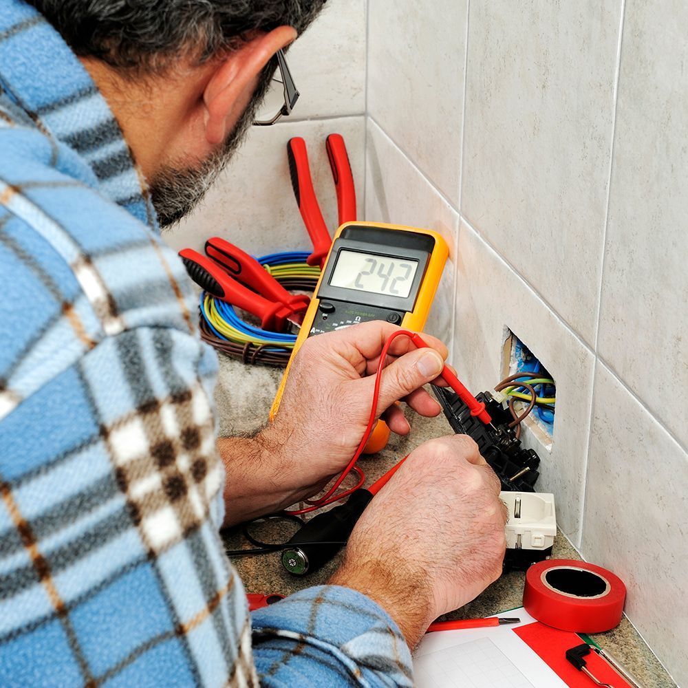 A man in a plaid shirt is using a multimeter with the number 242 on the screen