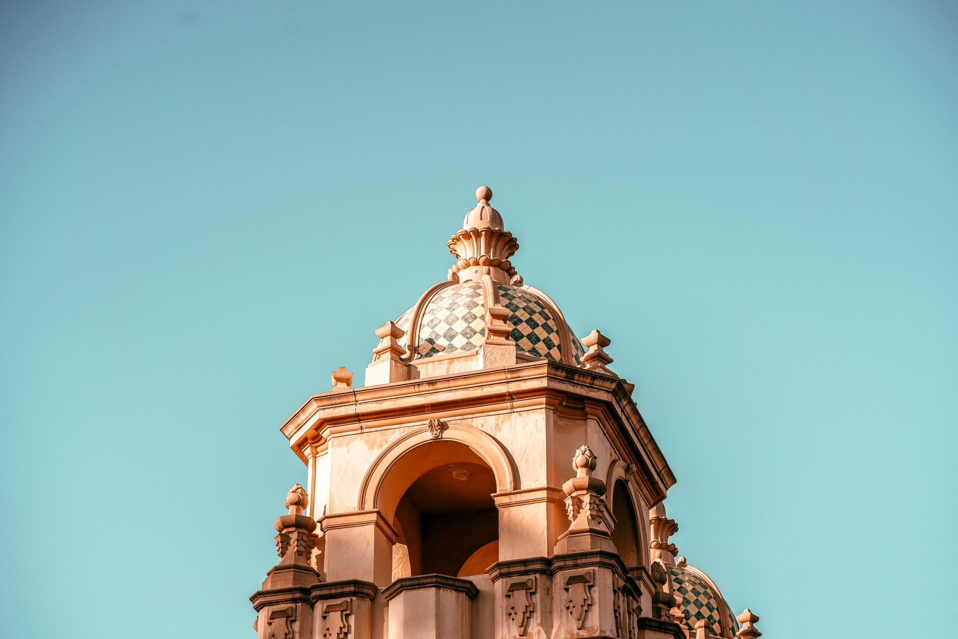 Ornate, light-colored tower with dome against a bright blue sky.