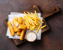 A wooden cutting board topped with fried fish and french fries.