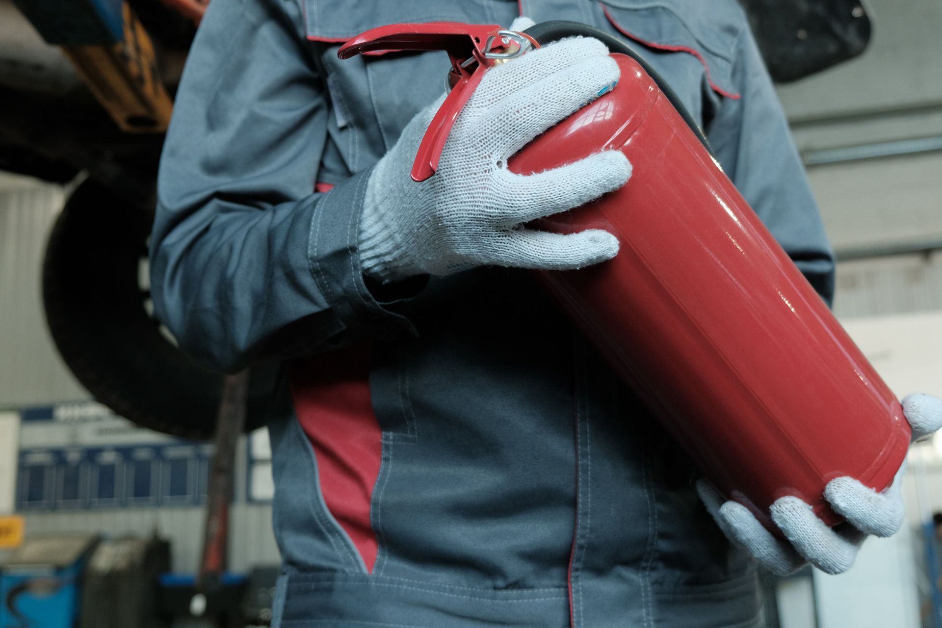 Technician holding red fire extinguisher before extinguisher recharge in auto repair shop. Technician holding red fire extinguisher before extinguisher recharge in auto repair shop.