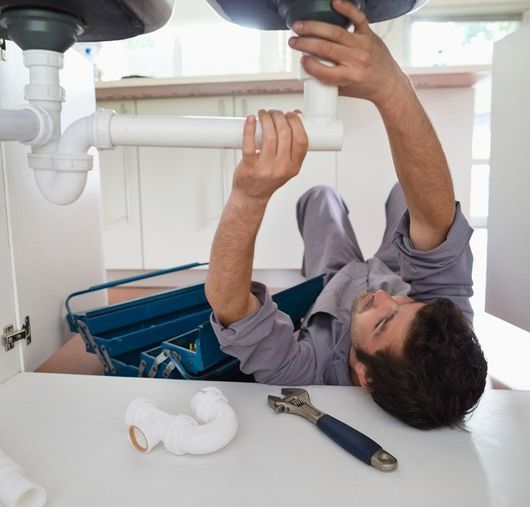 man working on plumbing under sink