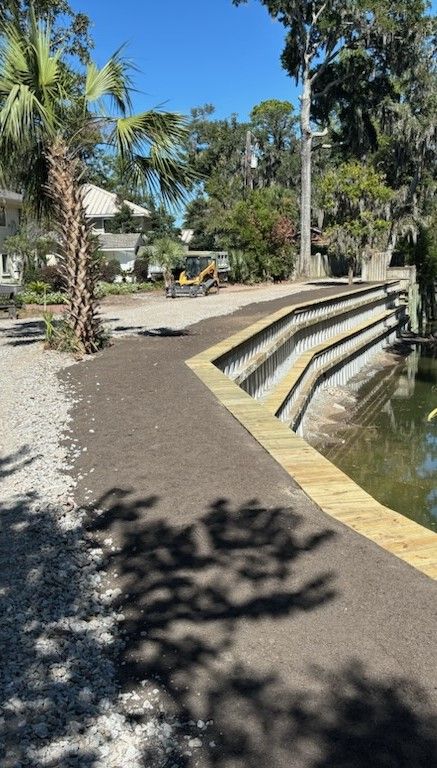 A shadow of a tree is cast on a wooden walkway next to a body of water.