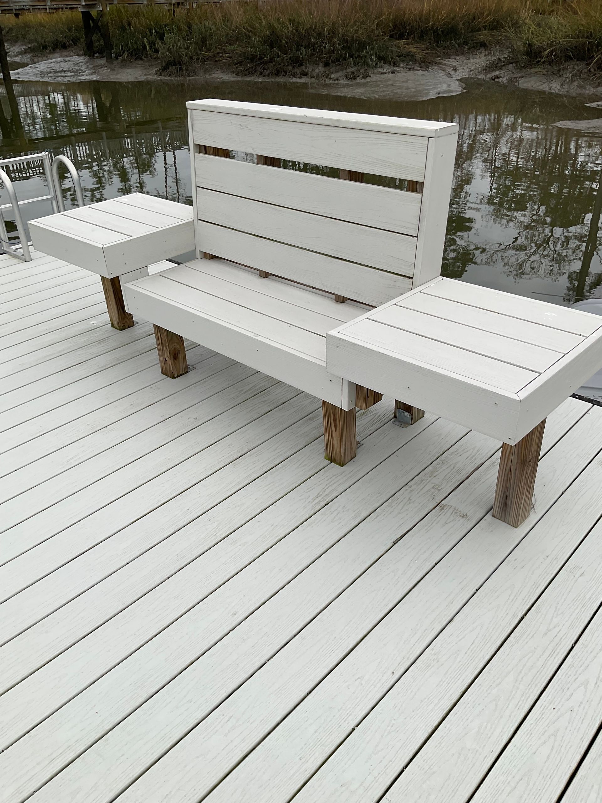 A white bench is sitting on a white deck next to a body of water.