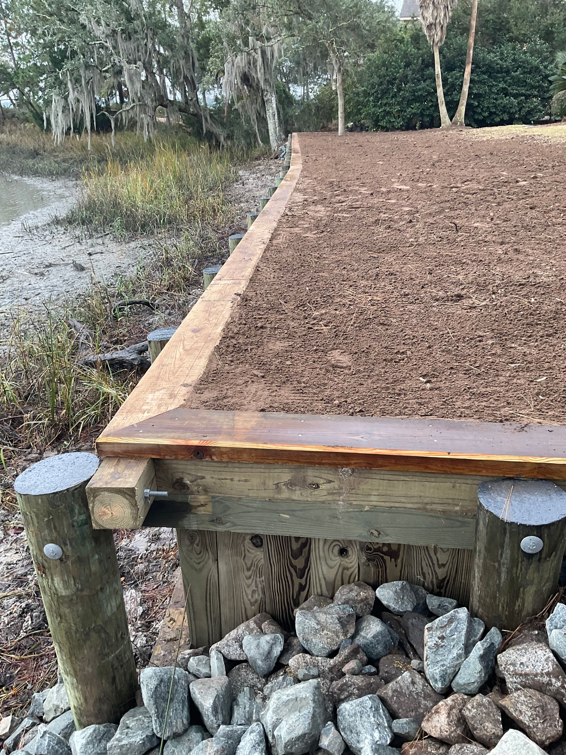 A wooden walkway surrounded by rocks and mulch next to a body of water.