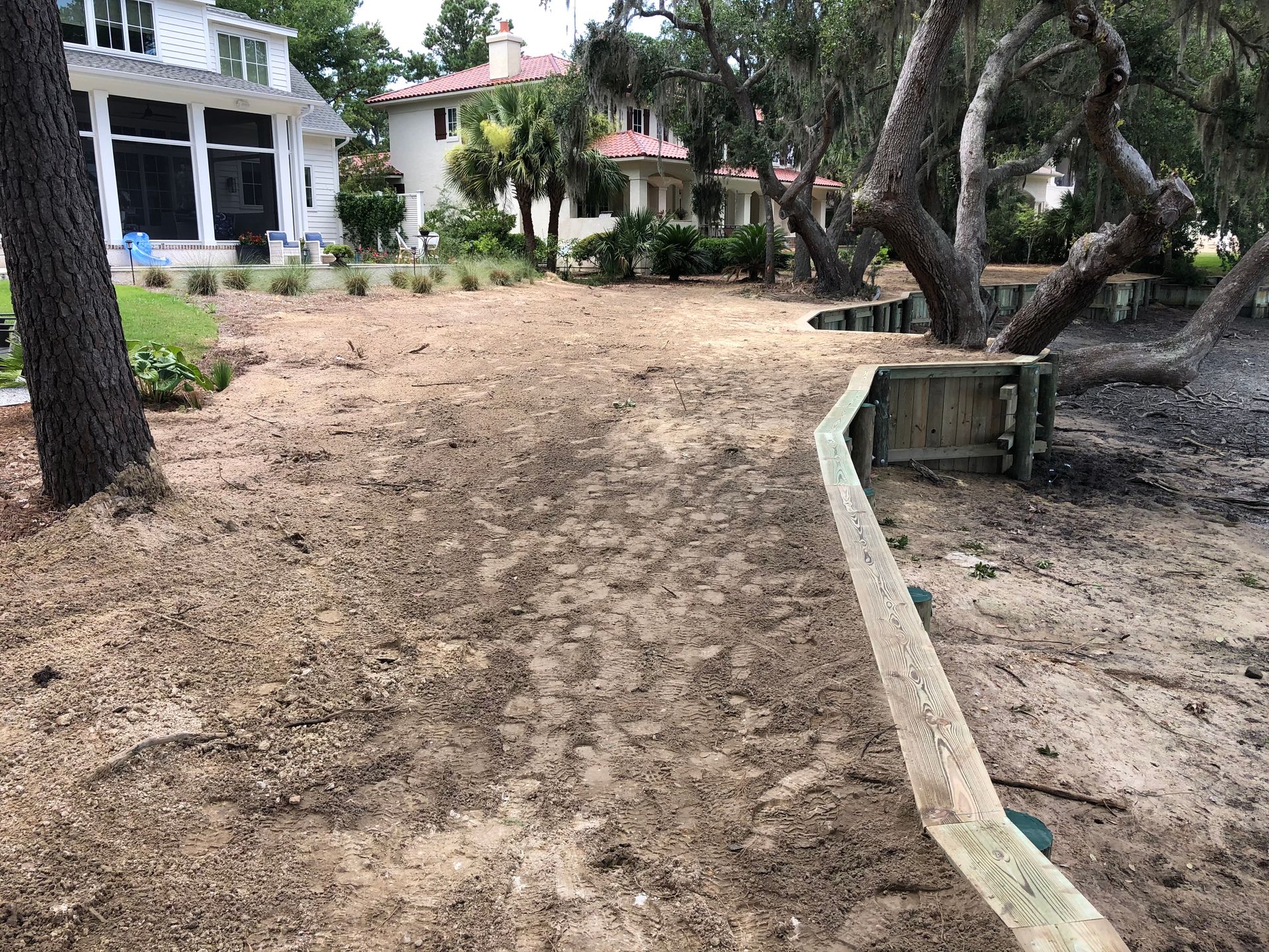 There is a wooden fence in the middle of a dirt field in front of a house.