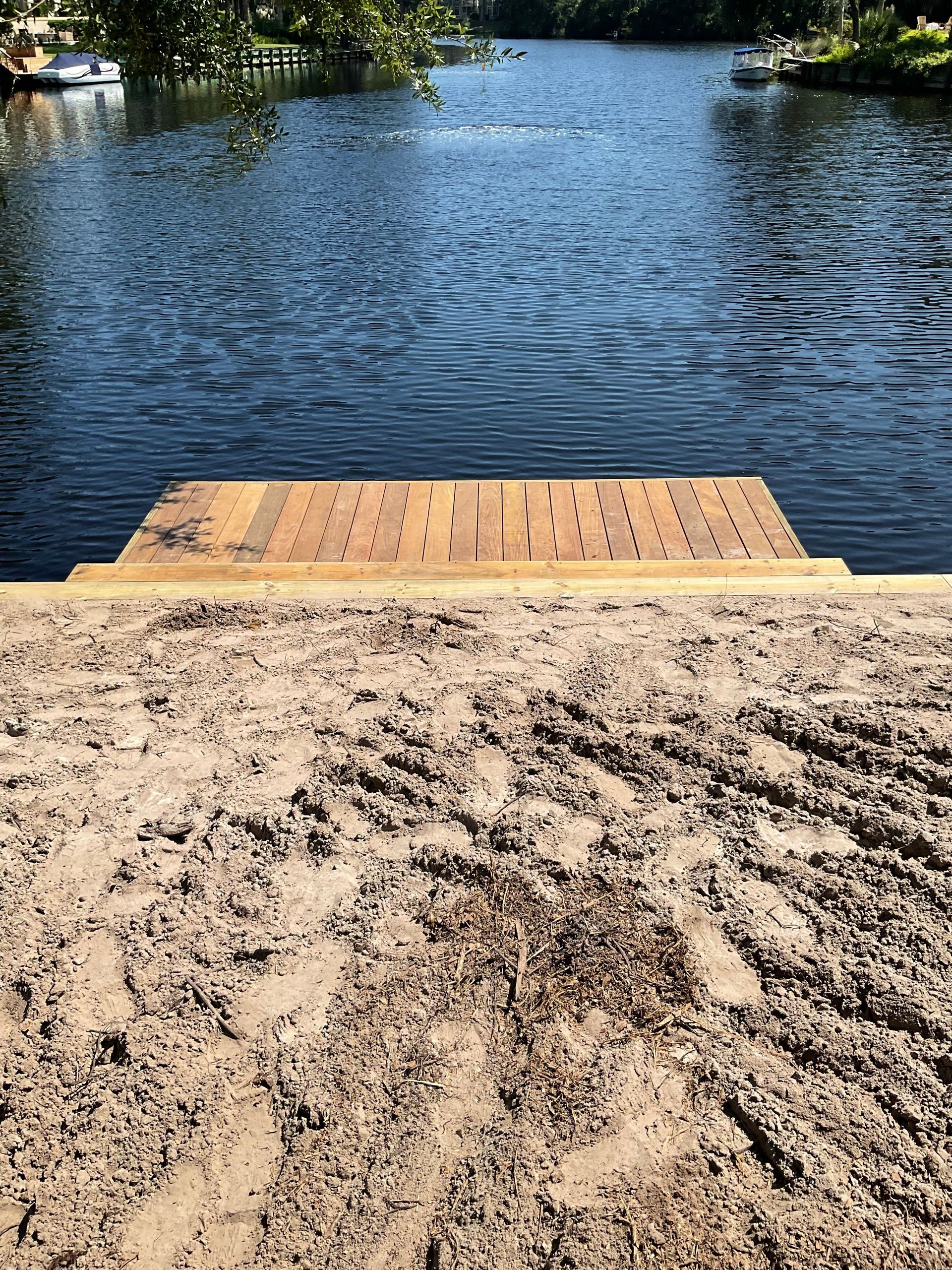 A wooden dock is sitting on top of a sandy beach next to a body of water.