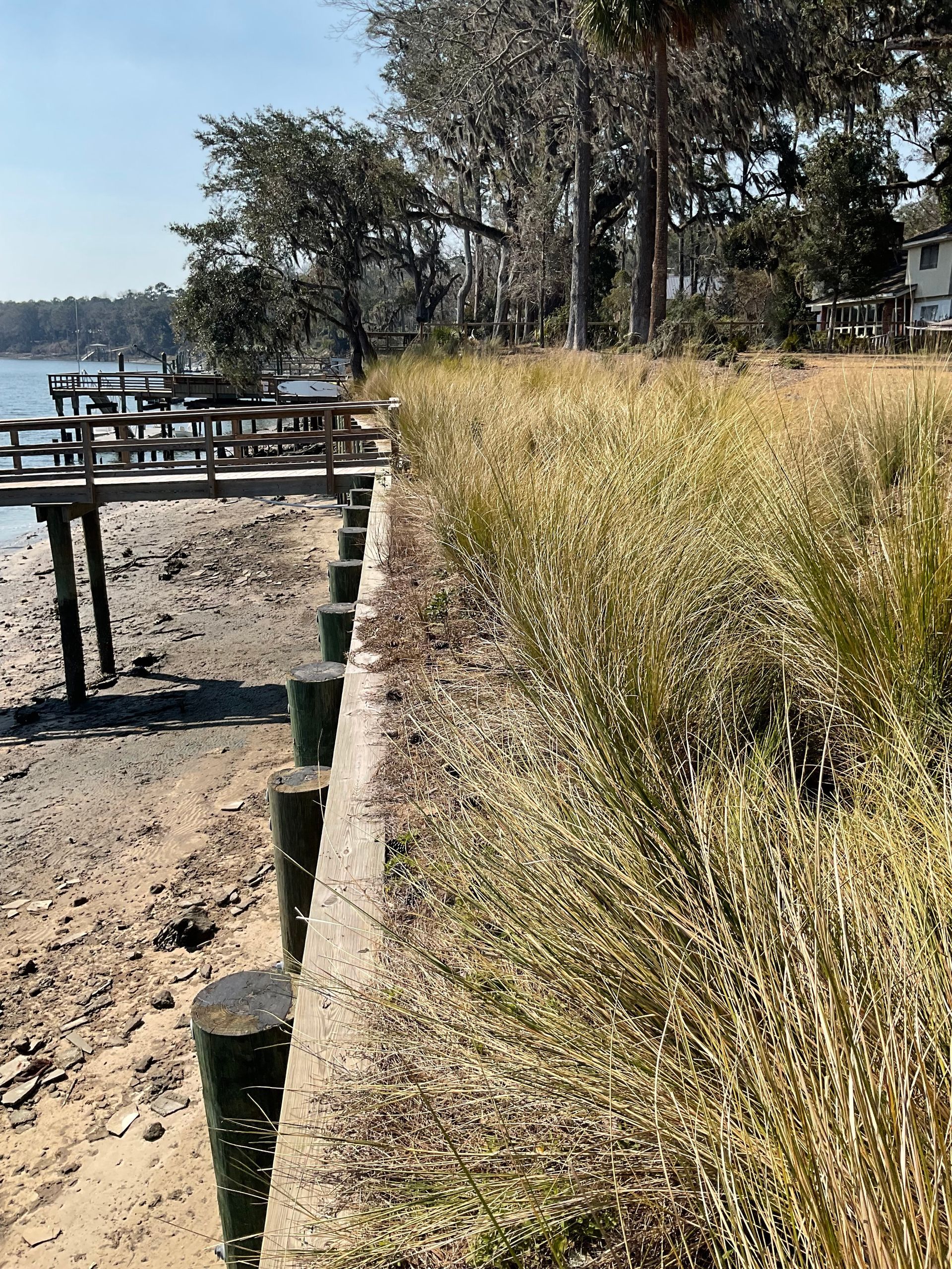 A wooden fence along a beach with a dock in the background.