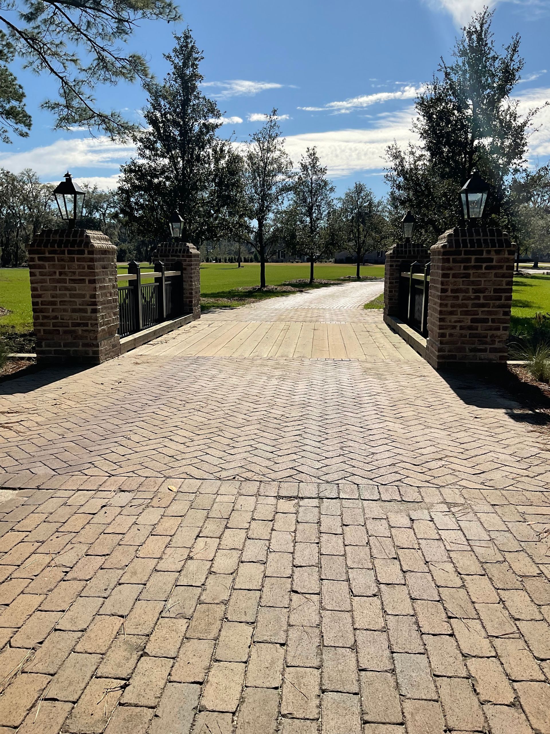 A brick driveway leading to a lush green field