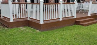 A deck with a white railing and stairs is sitting on top of a lush green lawn.