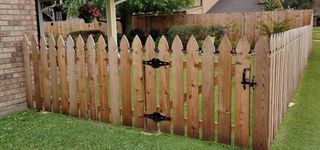 A wooden picket fence with a gate in front of a brick house.