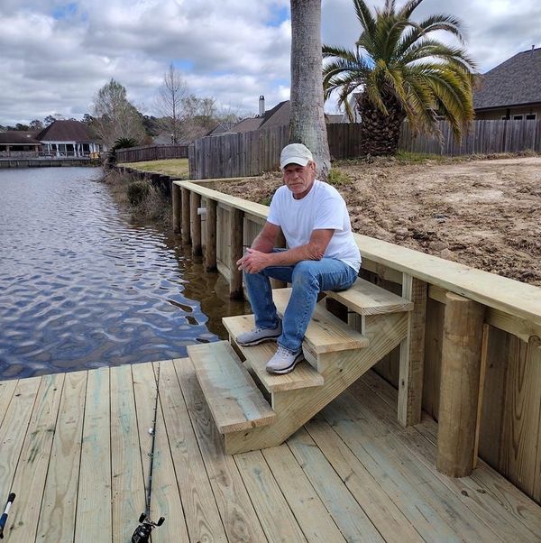 A man sits on the steps of a wooden dock overlooking a body of water