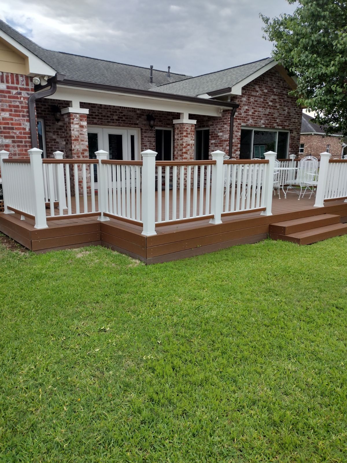 A large deck with a white railing is in front of a brick house.