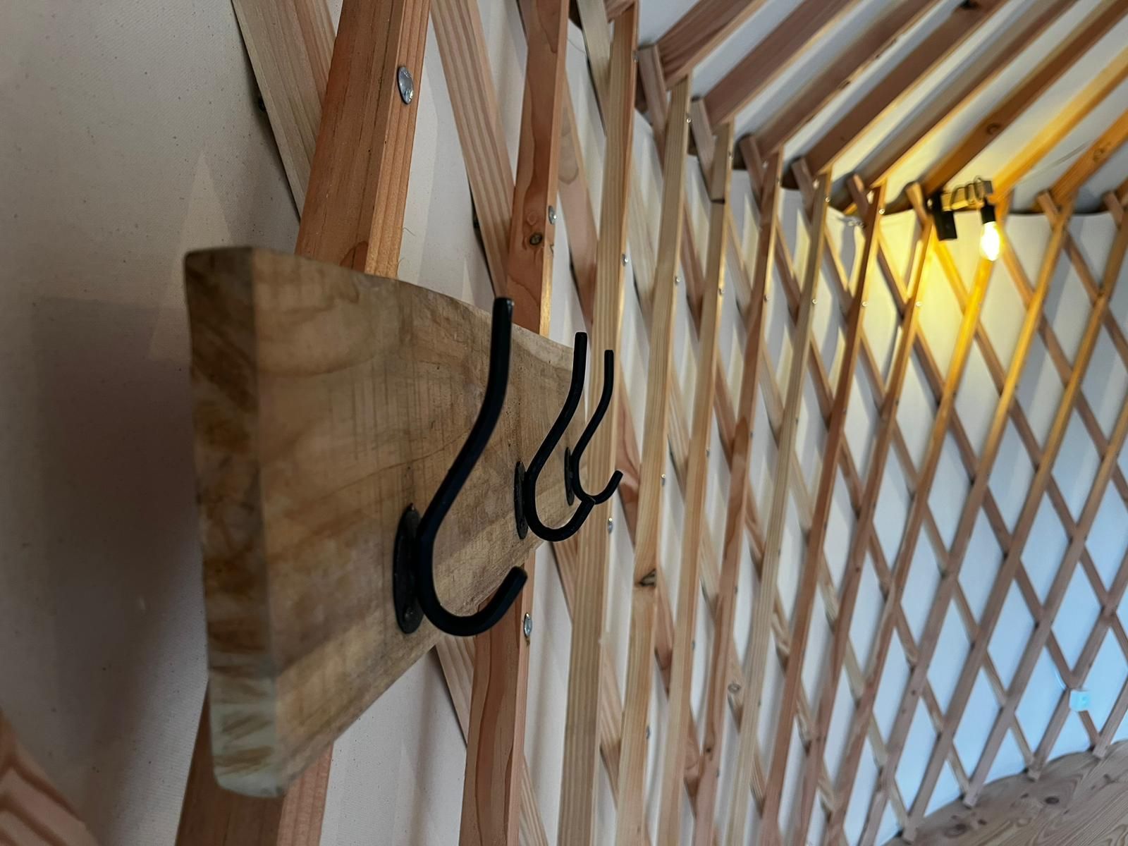 Porte-manteau en bois avec crochets noirs fixé au mur, à l'intérieur d'une yourte.