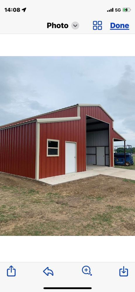 A red metal building with a white door and window is sitting in the middle of a grassy field.