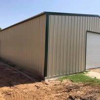 A large metal building with a garage door is sitting in the middle of a dirt field.