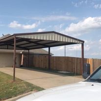 A car is parked under a metal carport in front of a house.