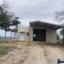 A metal building with a garage door is sitting on top of a dirt road.