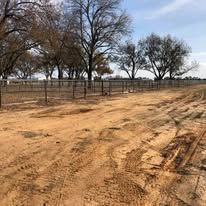 A dirt road leading to a fenced in area with trees in the background.