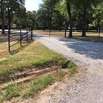 A dirt road going through a park with a fence and trees.