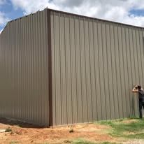 A man is standing in front of a large metal building.