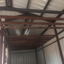 The inside of a metal building with wooden beams and a metal roof.