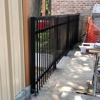 A black metal fence is being built next to a brick building.