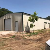 A large metal building with a garage door is sitting in the middle of a dirt field.
