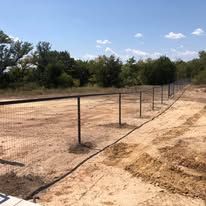A fence is surrounding a dirt field with trees in the background.