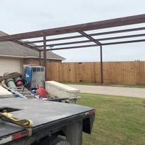 A truck is parked in front of a house with a wooden fence in the background.