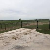 A fence surrounds a concrete driveway leading to a field.