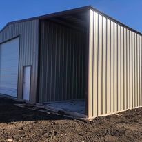 A metal building with a garage door is sitting on top of a dirt field.