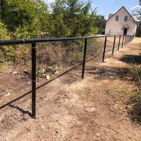 A black fence is sitting on top of a dirt path next to a house.
