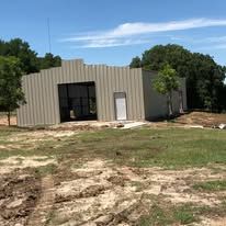 A large metal building is sitting in the middle of a grassy field.