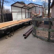 A trailer is sitting on top of a concrete driveway next to a wooden fence.
