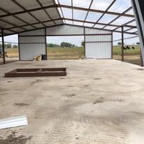 A large empty metal building with a cow in the background.