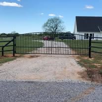 A black metal gate is sitting on the side of a gravel road.