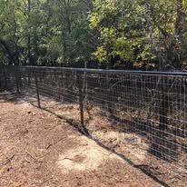 A wire fence surrounds a dirt path in the woods.