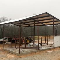 A metal shed is being built in the middle of a dirt field.