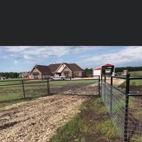 A fence surrounds a dirt road leading to a house.