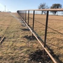 A long metal fence surrounds a dry grass field.