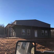 A large metal building is being built in the middle of a dirt field.