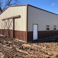 A metal building with a sliding barn door is sitting in the middle of a dirt field.