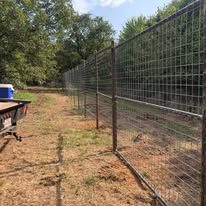 A fence is surrounding a dirt field with trees in the background.