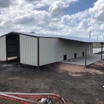 A metal building with a roof is sitting in the middle of a dirt field.